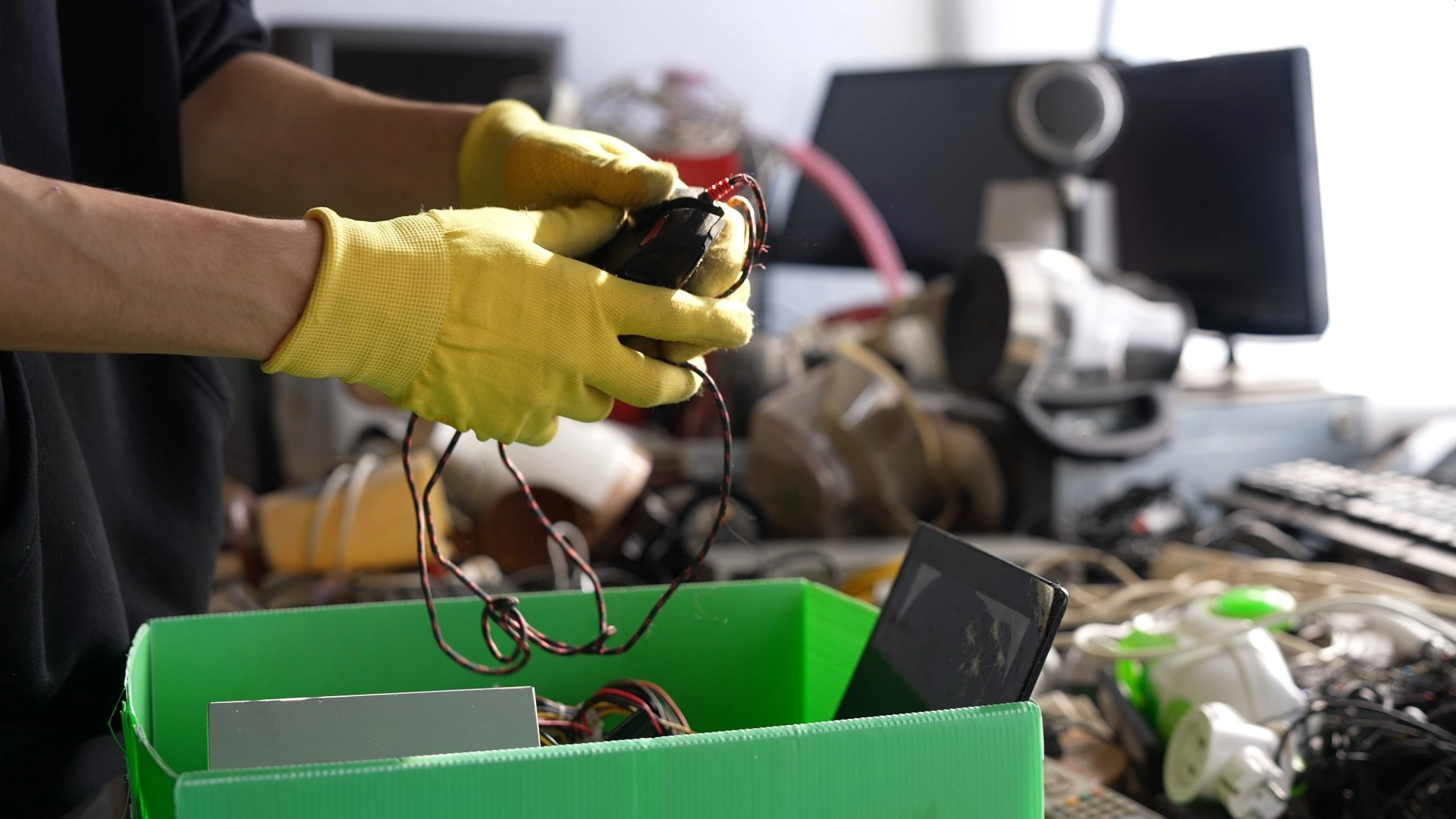 Worker in protective gloves sorting scrap cables and electronic components into a recycling bin